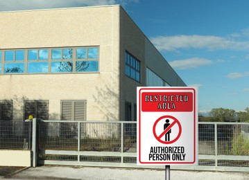 Image of Sign with text Restricted Area Authorized Person Only on fence near factory building outdoors
