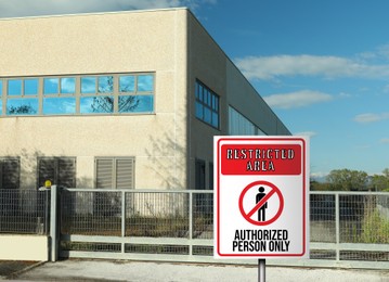 Sign with text Restricted Area Authorized Person Only on fence near factory building outdoors