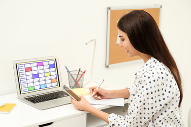 Photo of Young woman planning her schedule with calendar app on laptop in office