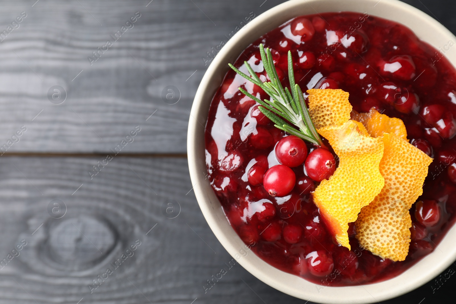 Photo of Fresh cranberry sauce, rosemary and orange peel in bowl on black wooden table, top view. Space for text