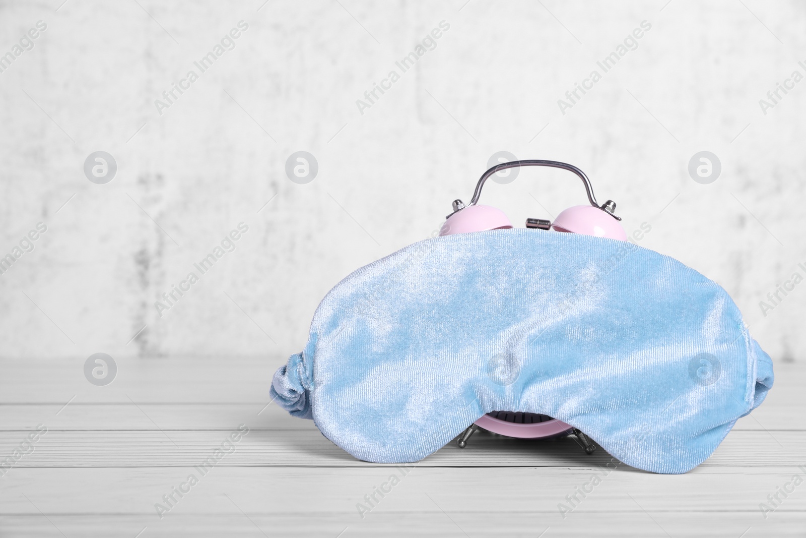 Photo of Soft sleep mask and alarm clock on white wooden table. Space for text