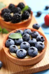 Photo of Tartlet with fresh blueberries on wooden board, closeup. Delicious dessert