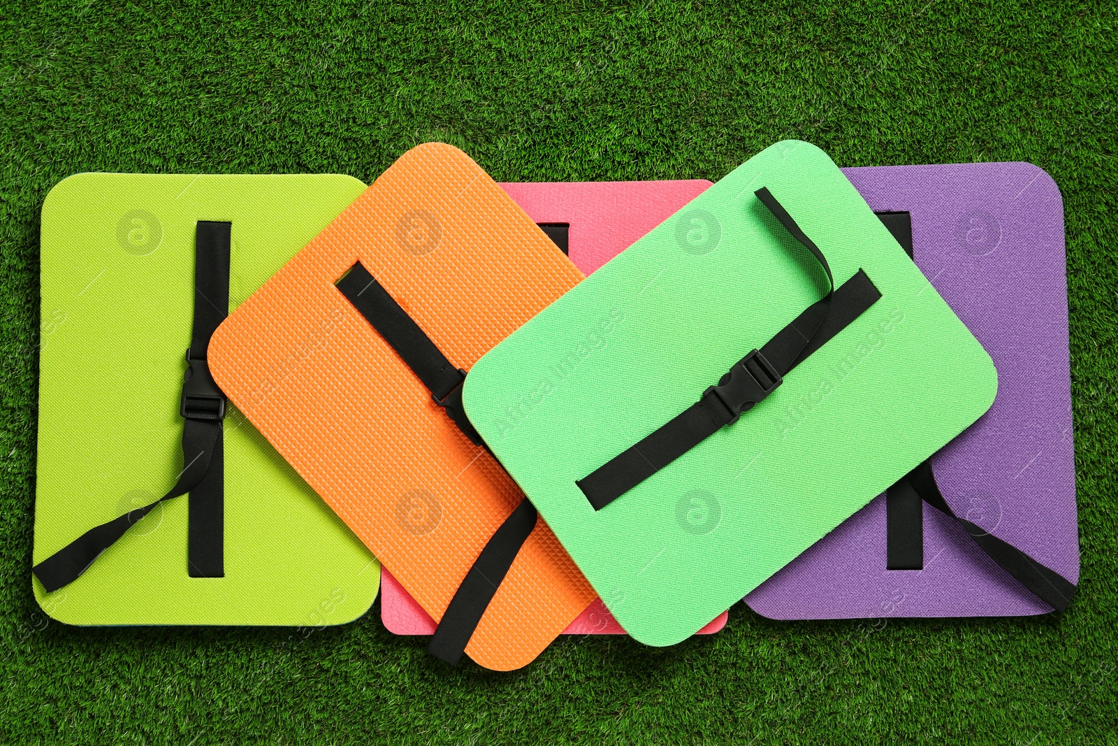 Photo of Bright foam tourist seat mats on green grass, flat lay