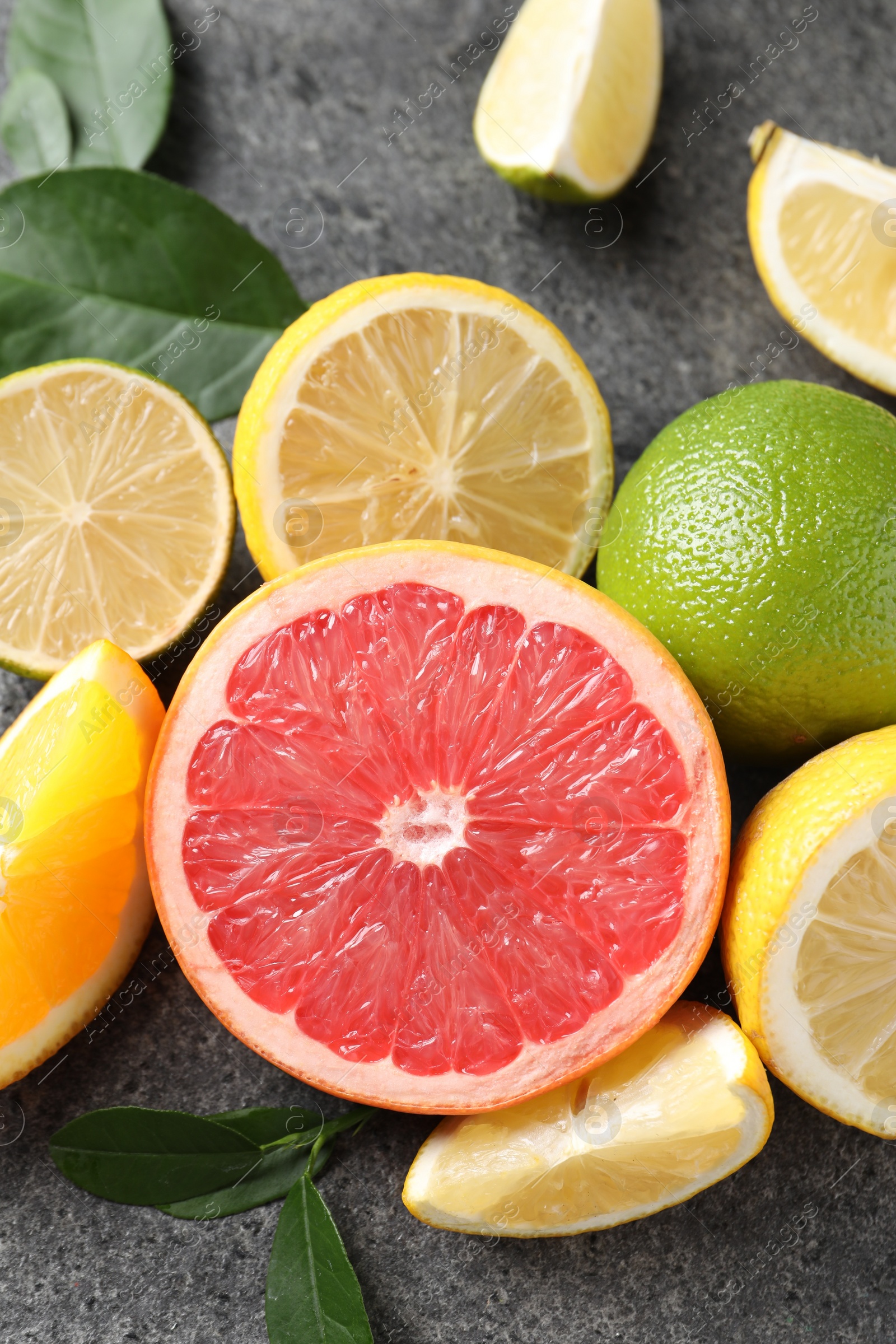 Photo of Different fresh citrus fruits and leaves on grey textured table, above view