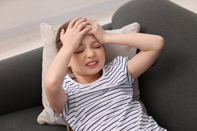 Photo of Little girl suffering from headache on sofa indoors