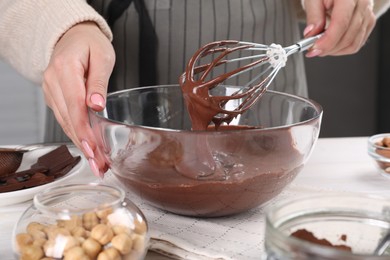 Woman mixing delicious chocolate cream with whisk at table indoors, closeup
