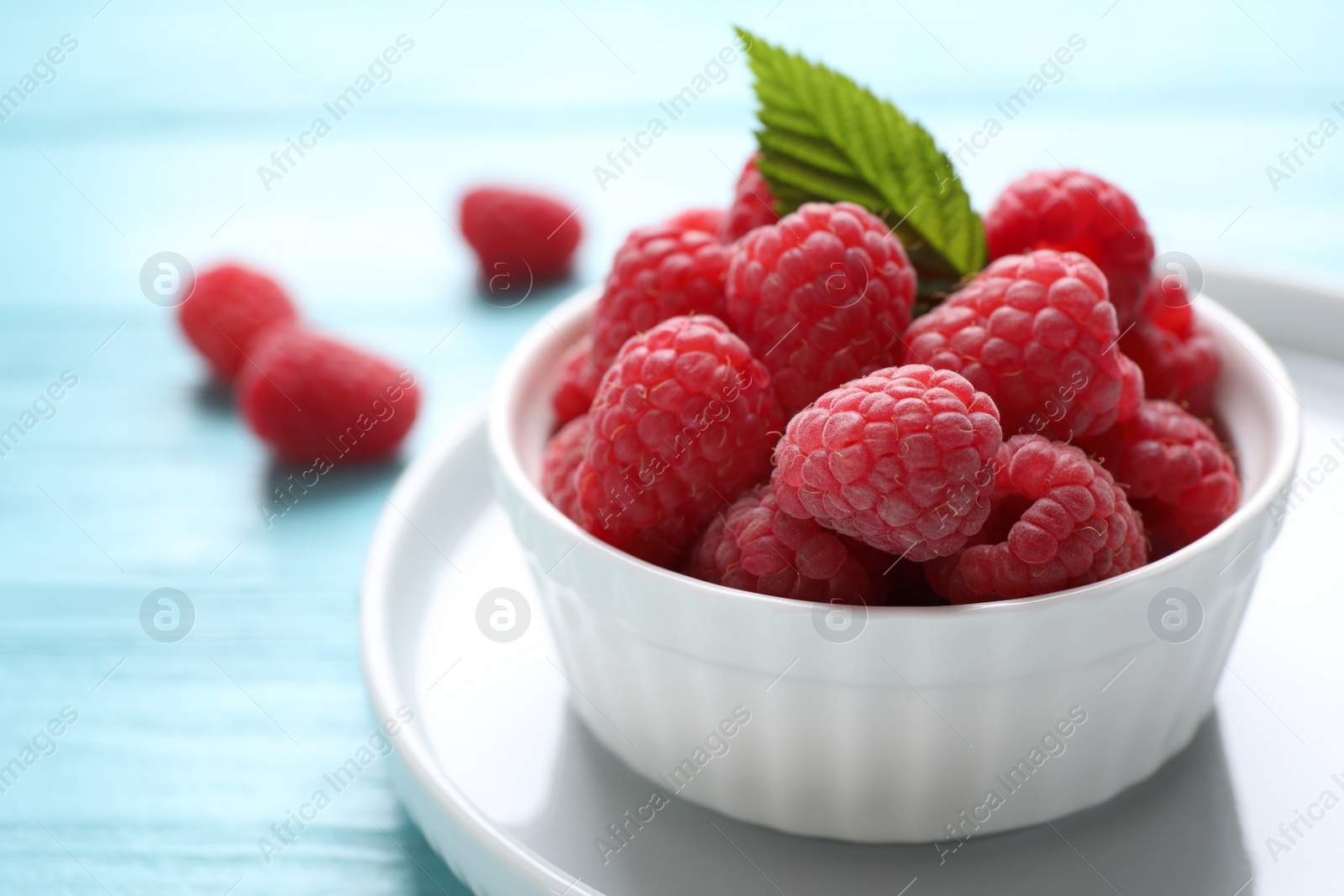 Photo of Delicious ripe raspberries in bowl on light blue wooden table, closeup