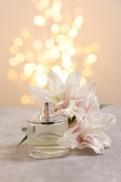 Photo of Bottle of perfume and beautiful lily flowers on table against beige background with blurred lights