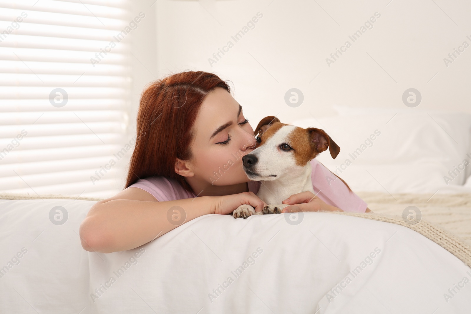 Photo of Woman kissing cute Jack Russell Terrier dog on bed at home