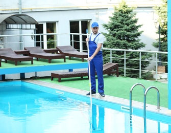 Photo of Male worker cleaning outdoor pool with scoop net