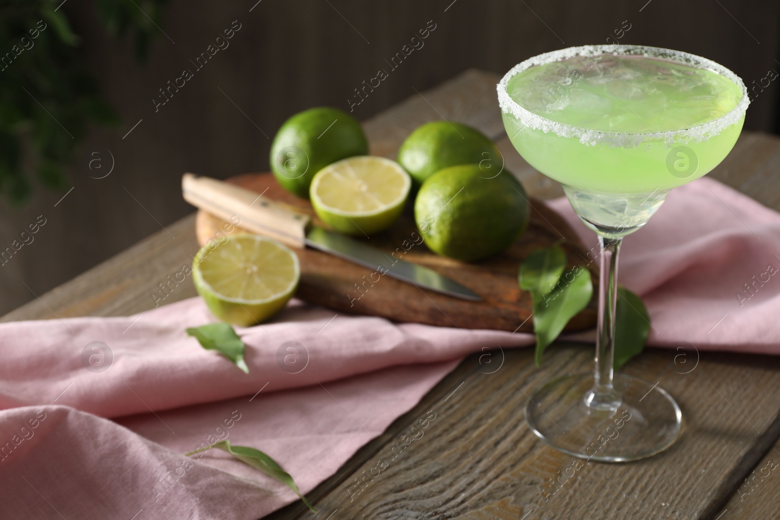 Photo of Delicious Margarita cocktail in glass, lime and leaves on wooden table, closeup