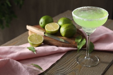 Photo of Delicious Margarita cocktail in glass, lime and leaves on wooden table, closeup