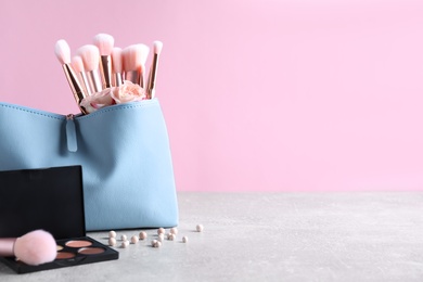 Photo of Bag with makeup brushes and cosmetic products on grey table against pink background. Space for text