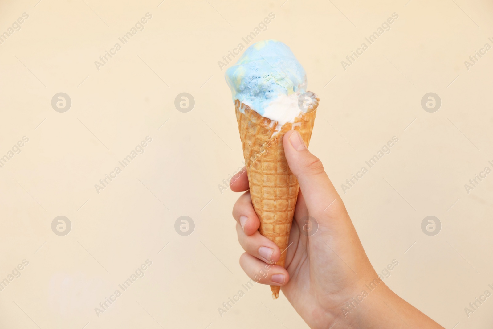 Photo of Woman holding delicious ice cream in wafer cone near beige wall outdoors, closeup