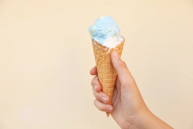 Woman holding delicious ice cream in wafer cone near beige wall outdoors, closeup