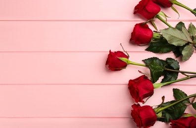 Photo of Beautiful red roses and space for text on pink wooden background, flat lay. Valentine's Day celebration
