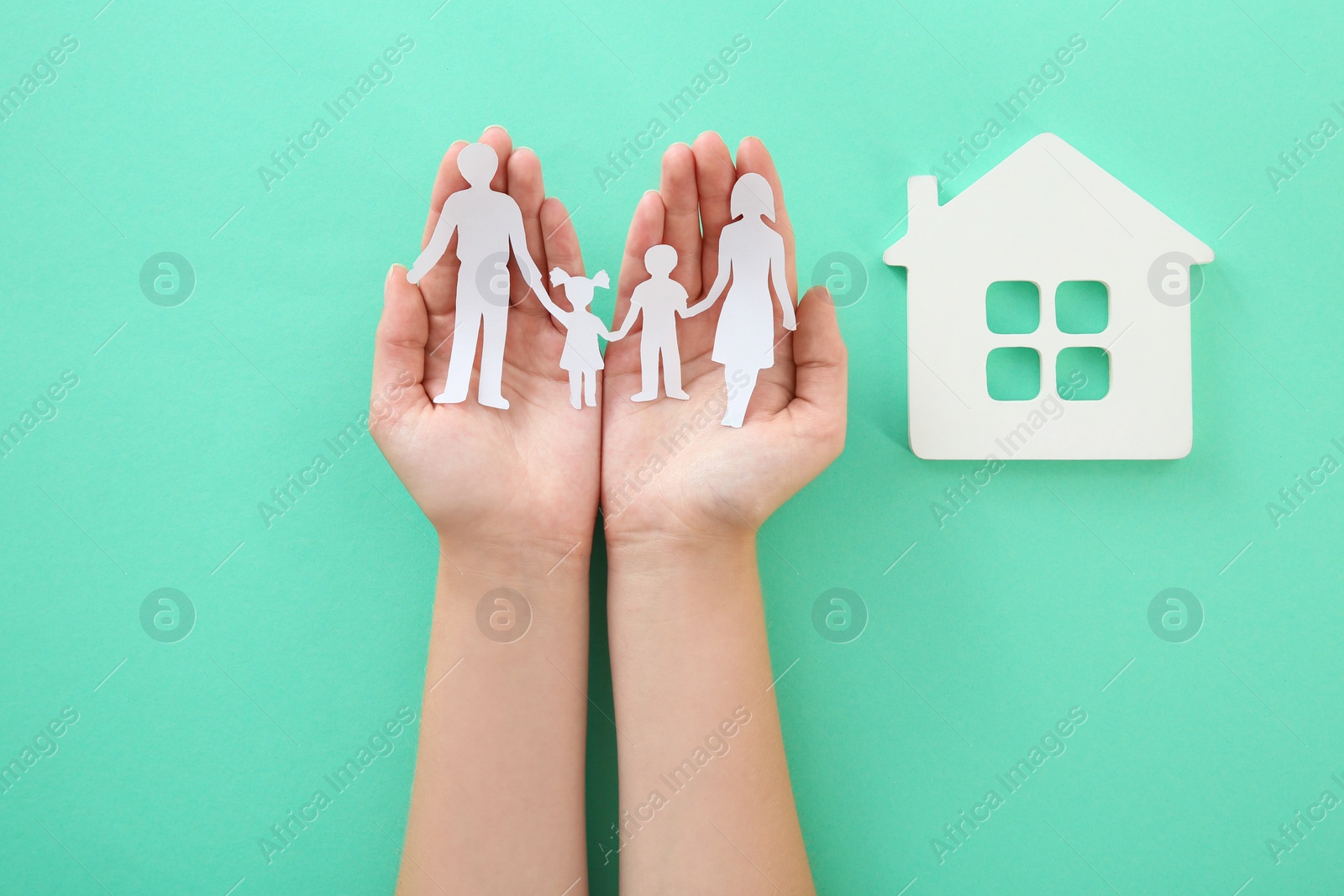 Photo of Woman holding paper family cutout near house model on color background, top view