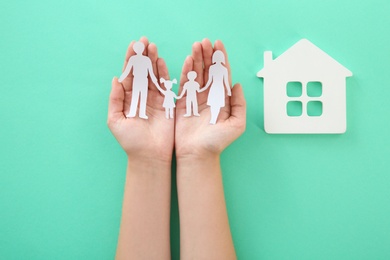 Woman holding paper family cutout near house model on color background, top view