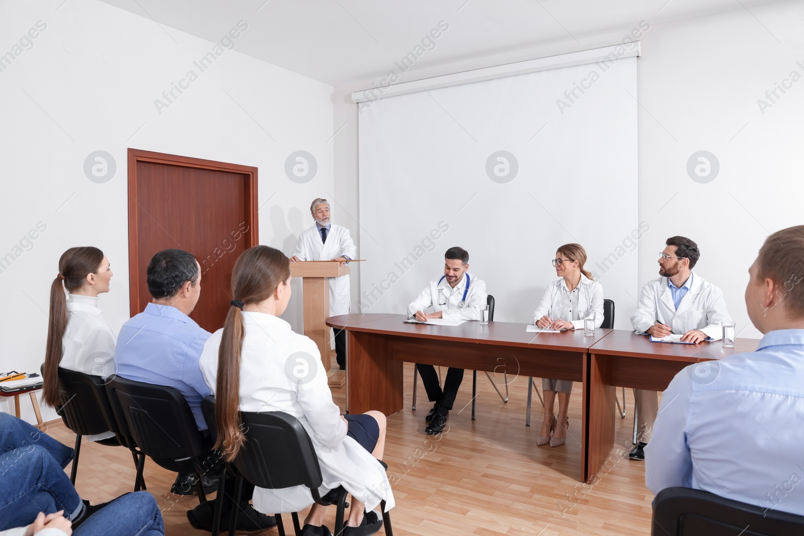 Photo of Senior doctor giving lecture in conference room with projection screen