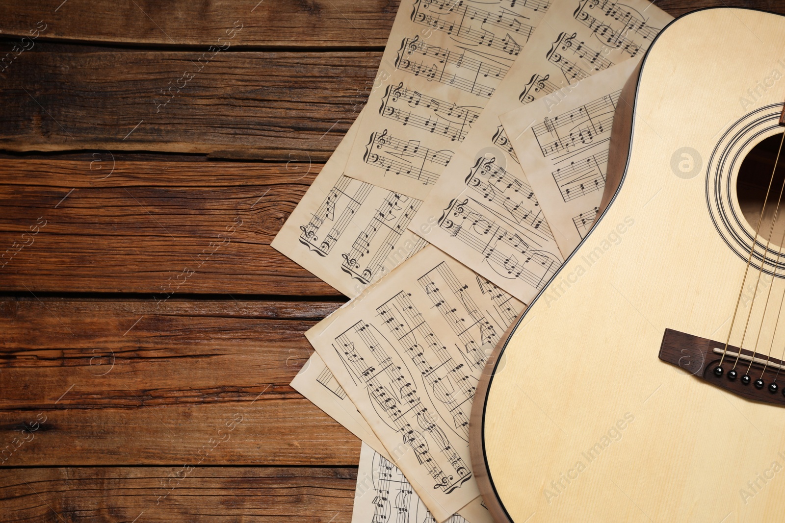 Photo of Paper sheets with music notes and acoustic guitar on wooden table, top view. Space for text