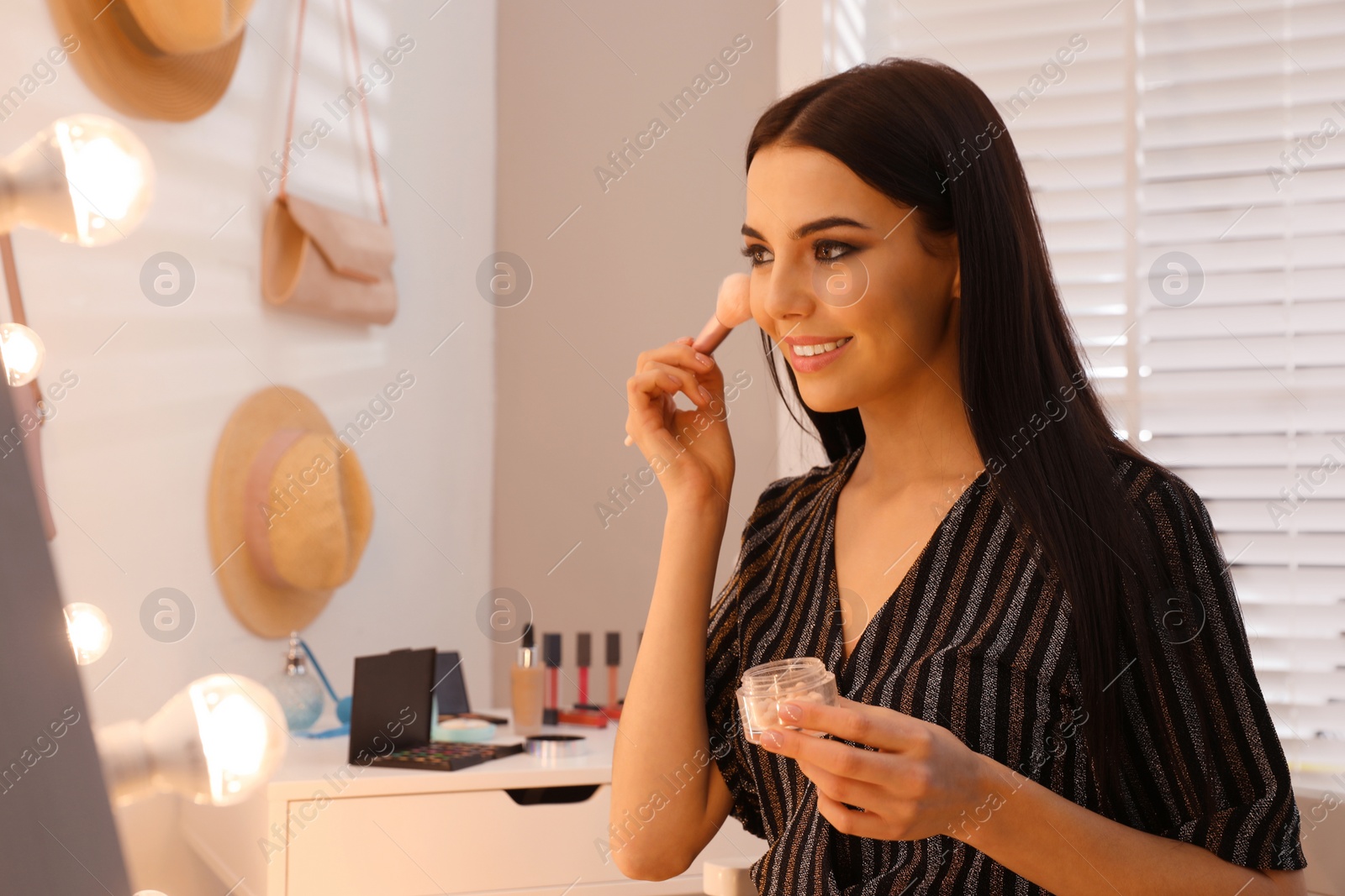 Photo of Beautiful young woman applying makeup near mirror in dressing room