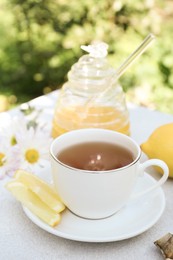 Cup of delicious tea with lemon and honey on white table outdoors