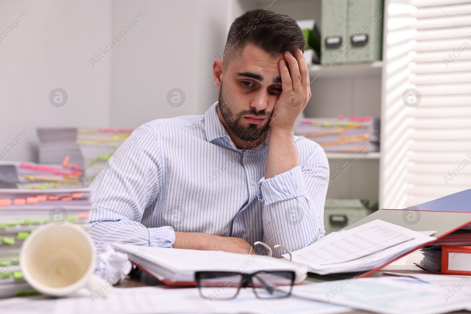 Photo of Overwhelmed man surrounded by documents at workplace in office