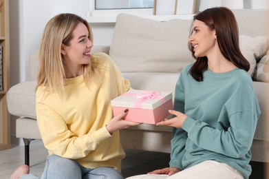 Photo of Smiling young woman presenting gift to her friend at home