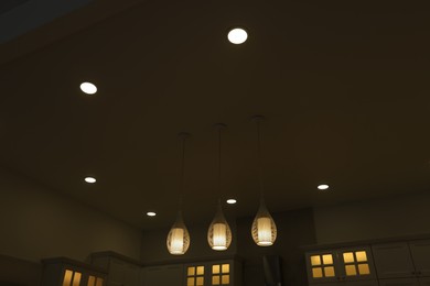 Photo of Ceiling with modern lamps and furniture in stylish kitchen at night, low angle view