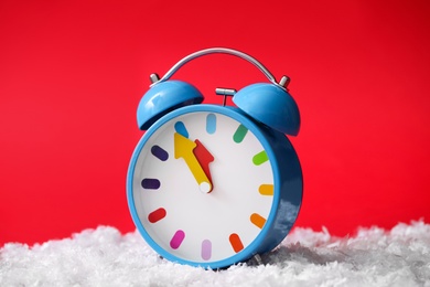 Photo of Alarm clock in pile of snow on red background. New Year countdown