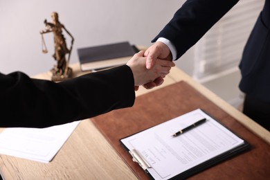 Notary shaking hands with client at wooden table in office, closeup