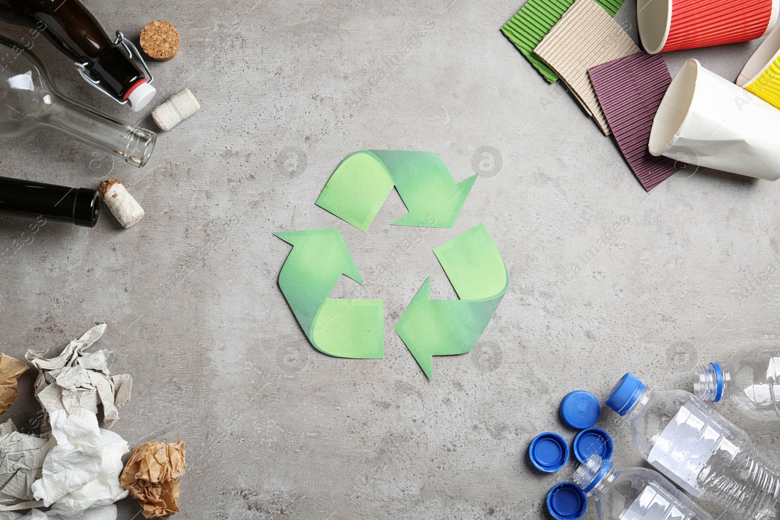 Photo of Recycling symbol and different garbage on gray background, top view