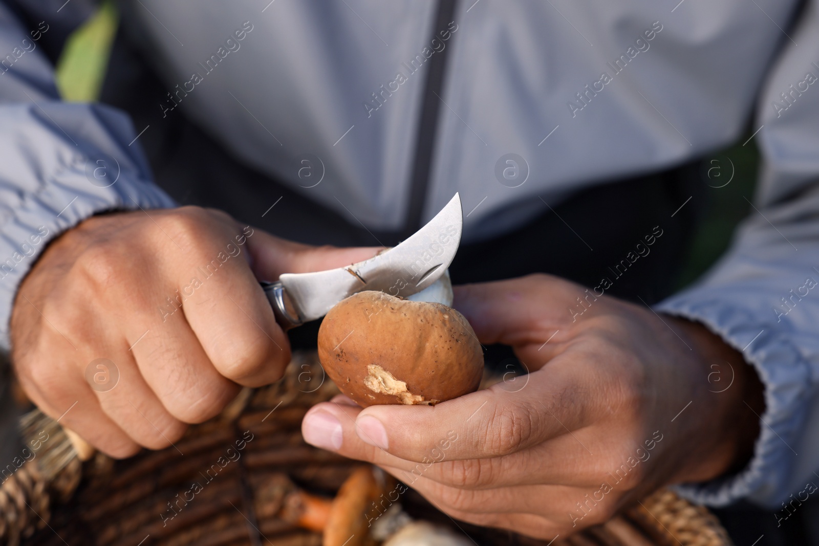 Photo of Man peeling mushroom with knife over basket, closeup