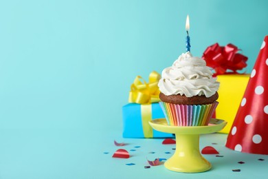 Photo of Delicious birthday cupcake with candle near gift boxes and party hat on light blue background, space for text