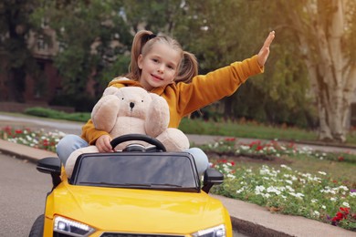 Cute little girl with toy bear driving children's car in park