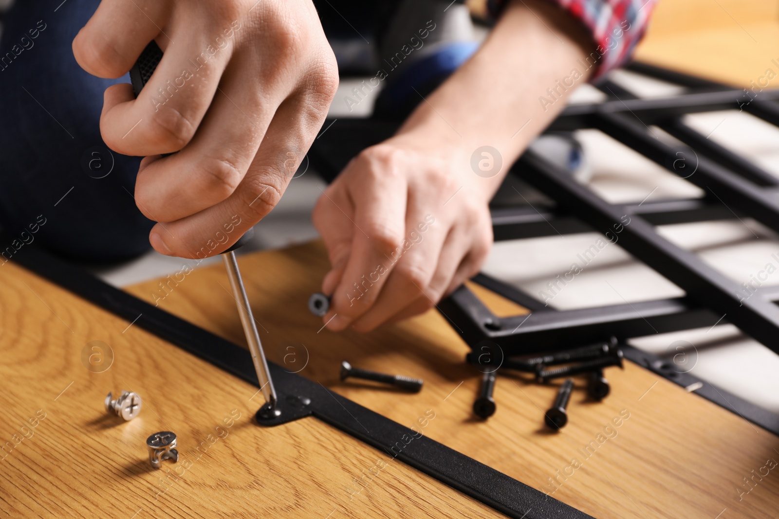 Photo of Man with screwdriver assembling wooden furniture indoors, closeup