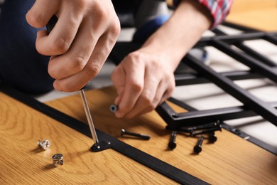 Man with screwdriver assembling wooden furniture indoors, closeup