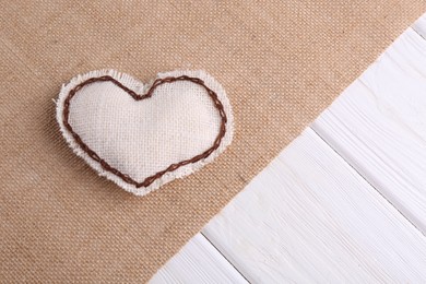 Heart made of burlap fabric with brown stitches and cloth on wooden table, top view. Space for text