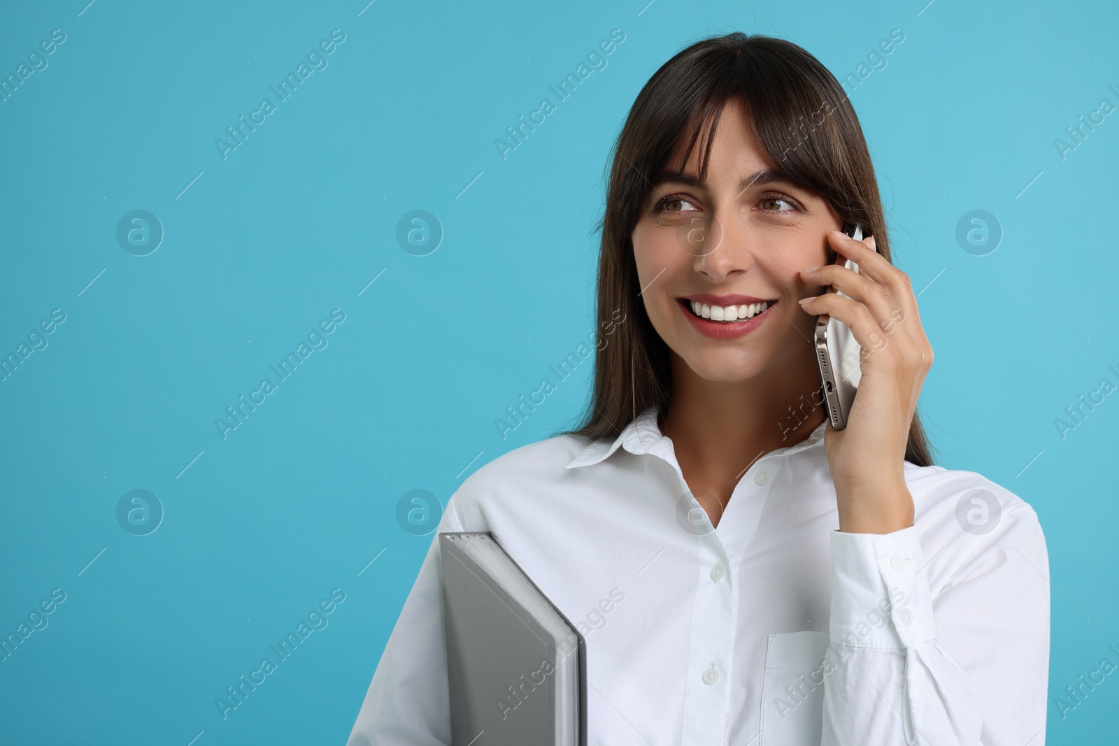 Photo of Happy secretary with folder talking on smartphone against light blue background. Space for text