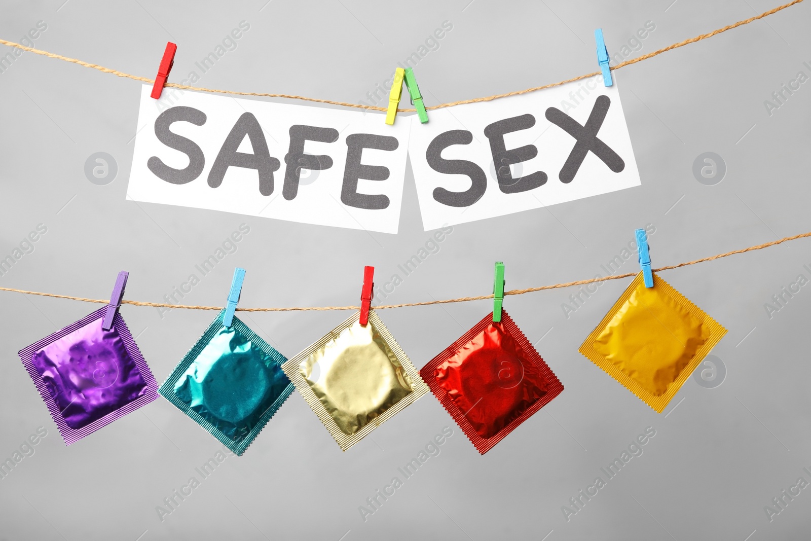 Photo of Paper sheets with words SAFE SEX and colorful condoms hanging on clothesline against light grey background