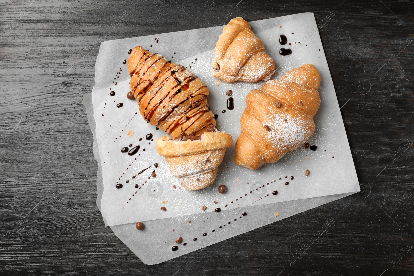 Photo of Tasty croissants with sugar powder and chocolate sauce on wooden background, top view