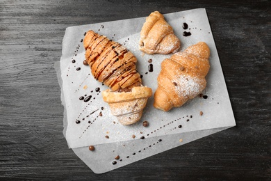 Tasty croissants with sugar powder and chocolate sauce on wooden background, top view