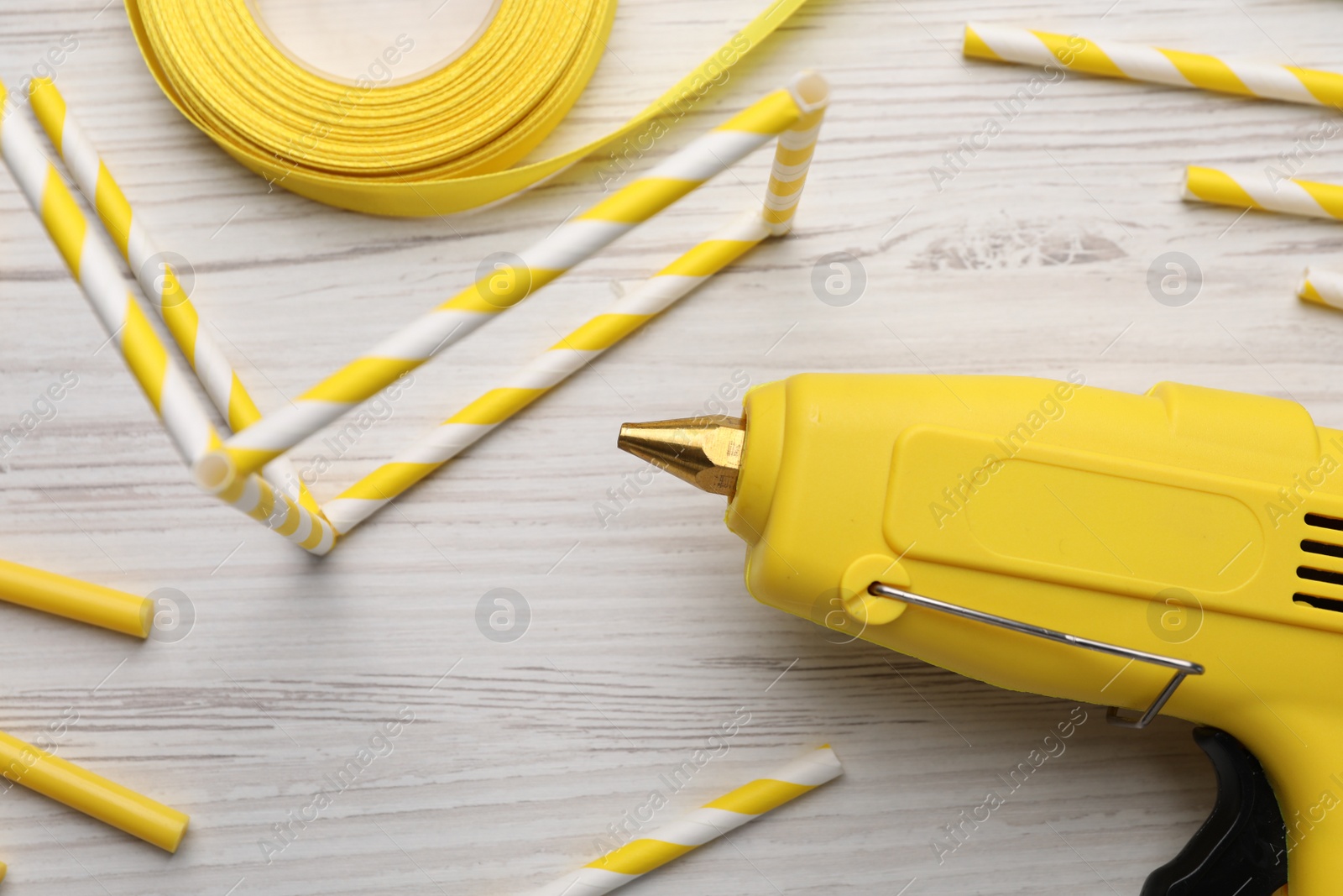 Photo of Hot glue gun and handicraft materials on white wooden table, flat lay