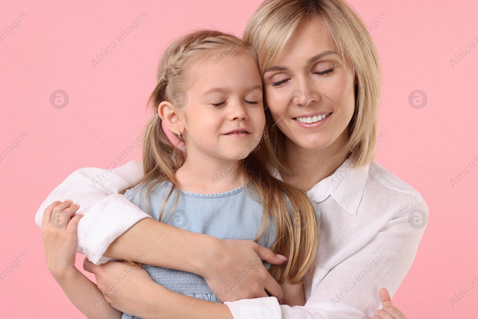 Photo of Mother hugging her happy daughter on pink background