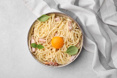 Photo of Bowl of tasty pasta Carbonara with basil leaves and egg yolk on light grey table, top view