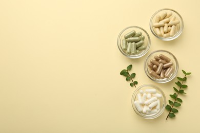 Different vitamin capsules in bowls and branches on pale yellow background, flat lay. Space for text