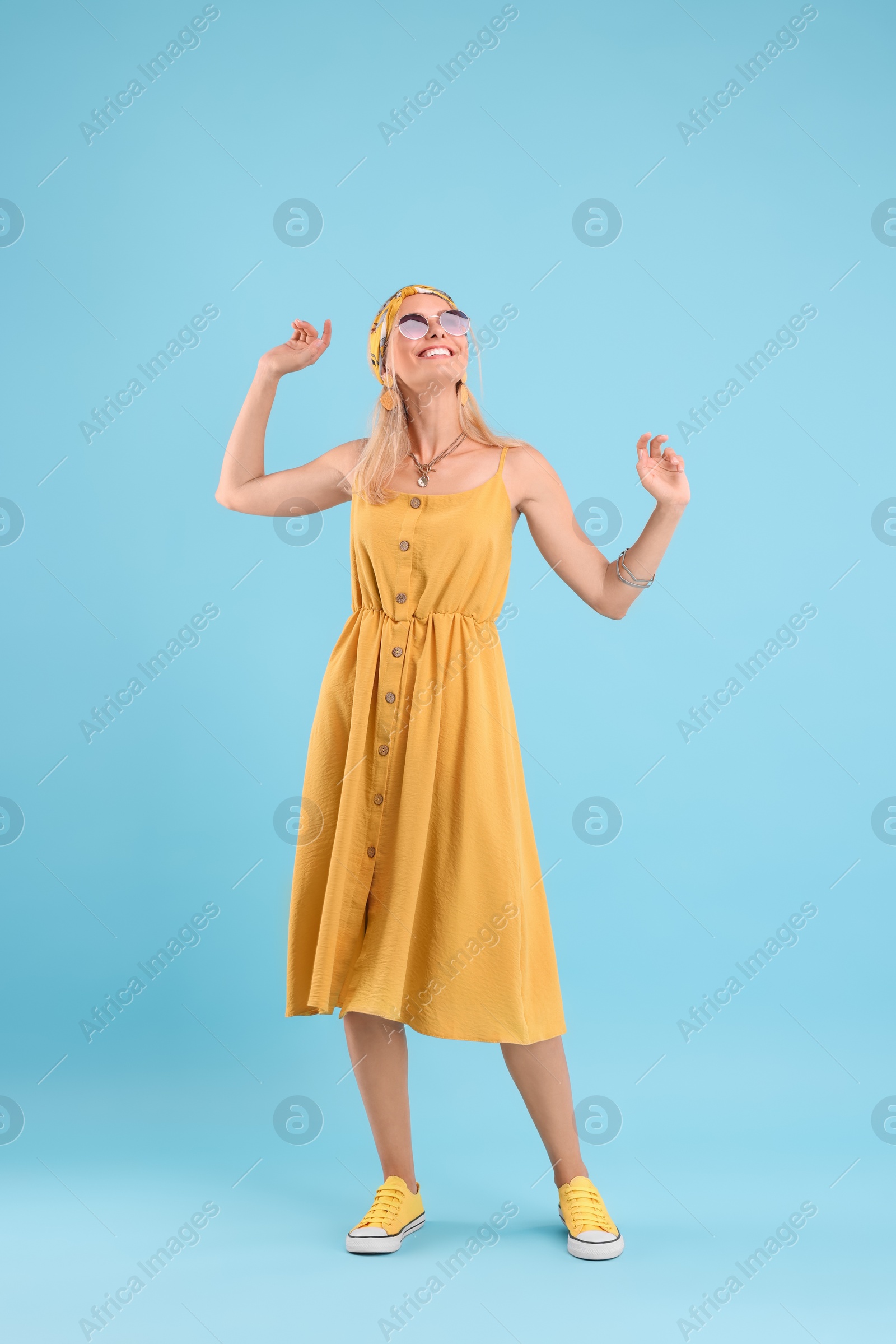 Photo of Portrait of smiling hippie woman dancing on light blue background