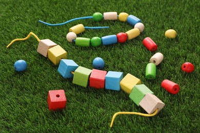 Photo of Wooden pieces and strings for threading activity on artificial grass, closeup. Educational toy for motor skills development