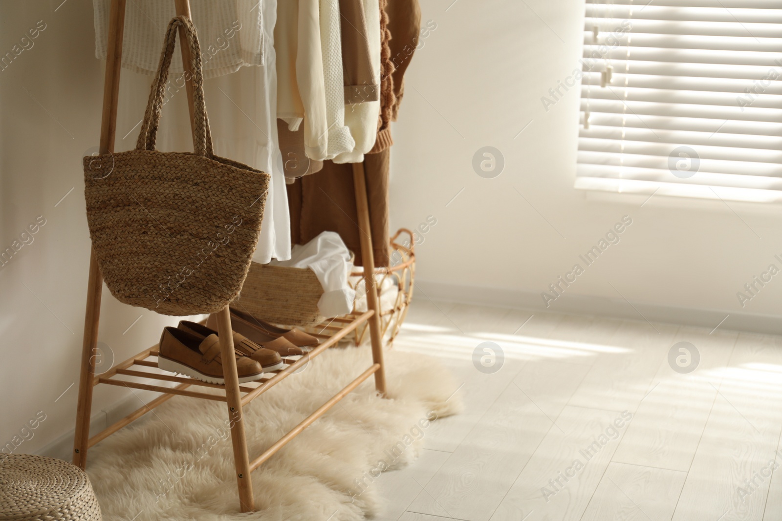 Photo of Rack with stylish bag and women's clothes in dressing room. Modern interior design