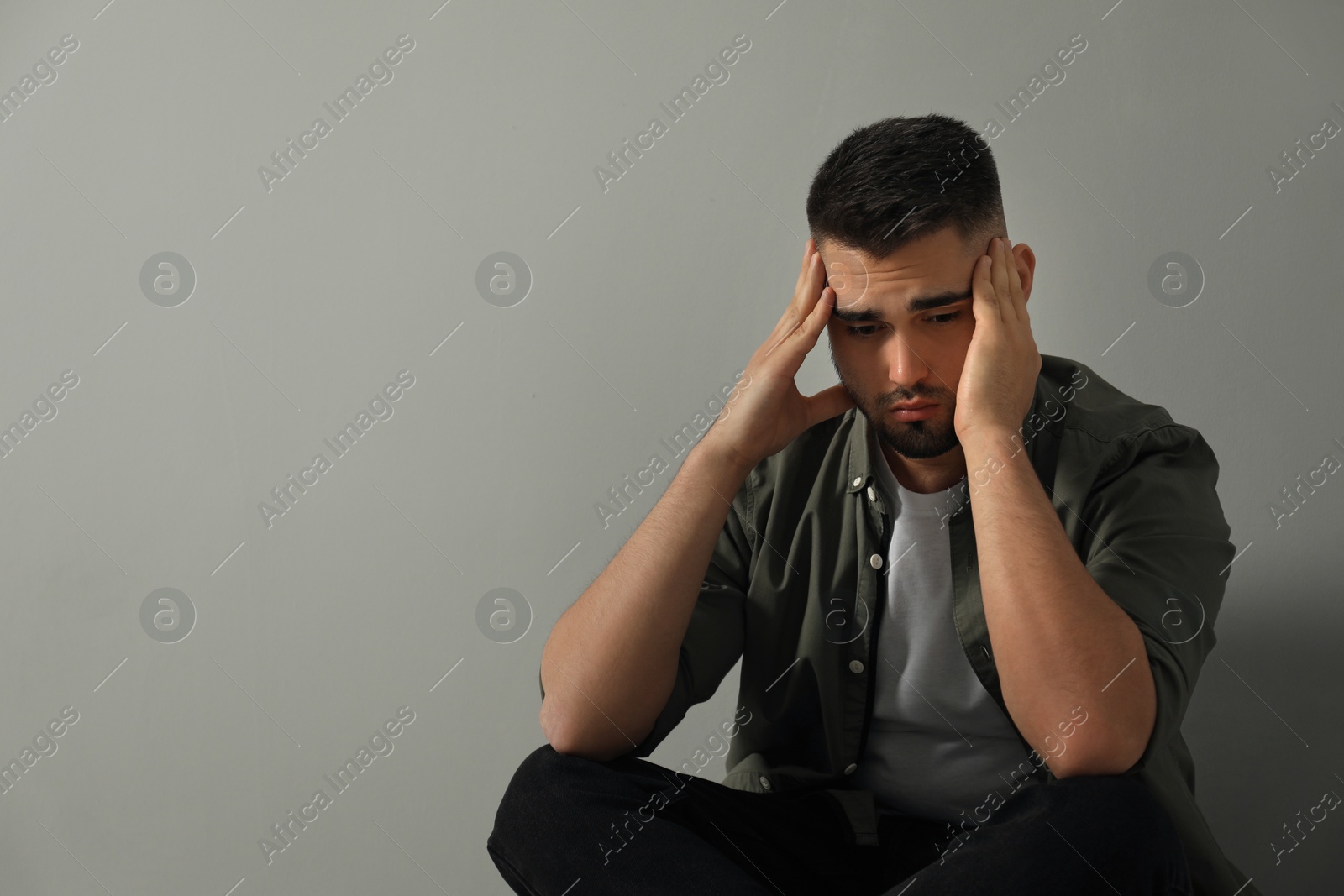 Photo of Sad man sitting near light grey wall. Space for text